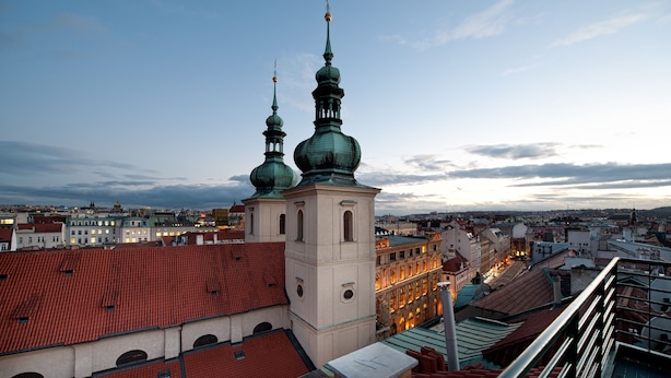 A high vantage point view of a cityscape with prominent green domed towers and a large building with a red-tiled roof. - Hotel Leon D´Oro (Prague)