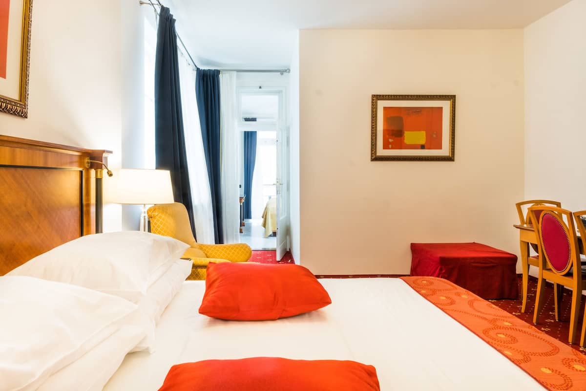 A hotel room with a bed, a desk, a chair, a lamp, and a painting on the wall.