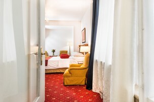 Quarto de hotel com cama, uma cadeira, um abajur e um tapete vermelho.