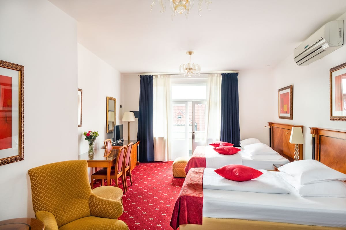A hotel room with two beds, a desk, a chair, and a chandelier.