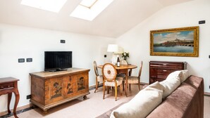 A living room with a television, wooden cabinet, dining table with chairs, a sofa, and a painting on the wall. - Hotel Leon D´Oro (Prague)