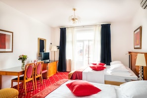 Una habitación de hotel con cama, escritorio con silla, televisor y ventana con cortinas.