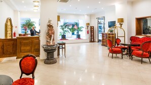 A spacious lobby with a reception desk, a statue, red upholstered chairs, and a large window with plants. - Hotel Leon D´Oro (Prague)