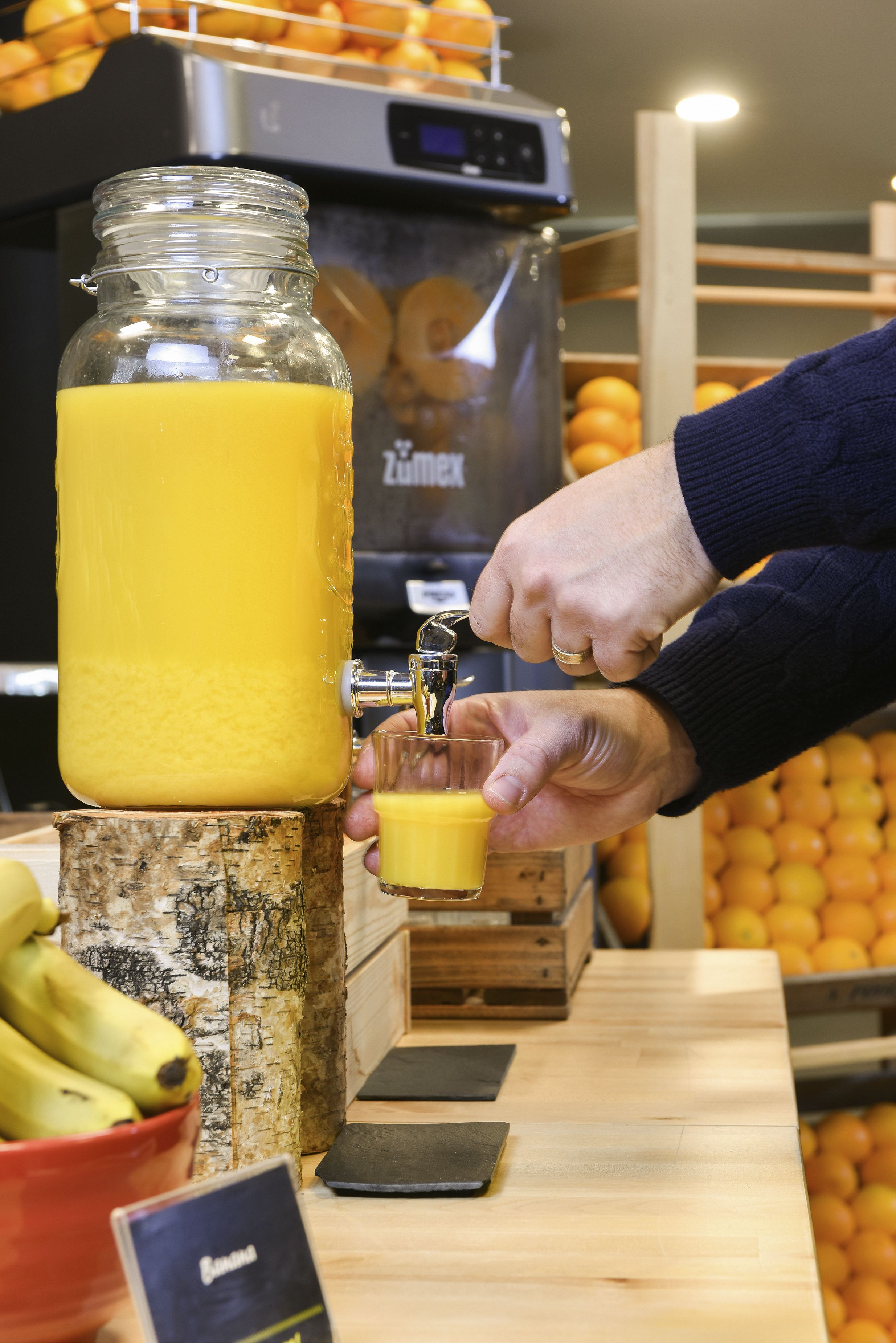 A person pouring orange juice from a large dispenser into a glass.