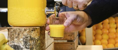 A person pouring orange juice from a large dispenser into a glass.