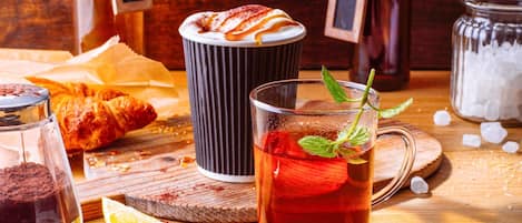 Una mesa con una taza de té, un croissant, una taza de café y un frasco de azúcar.