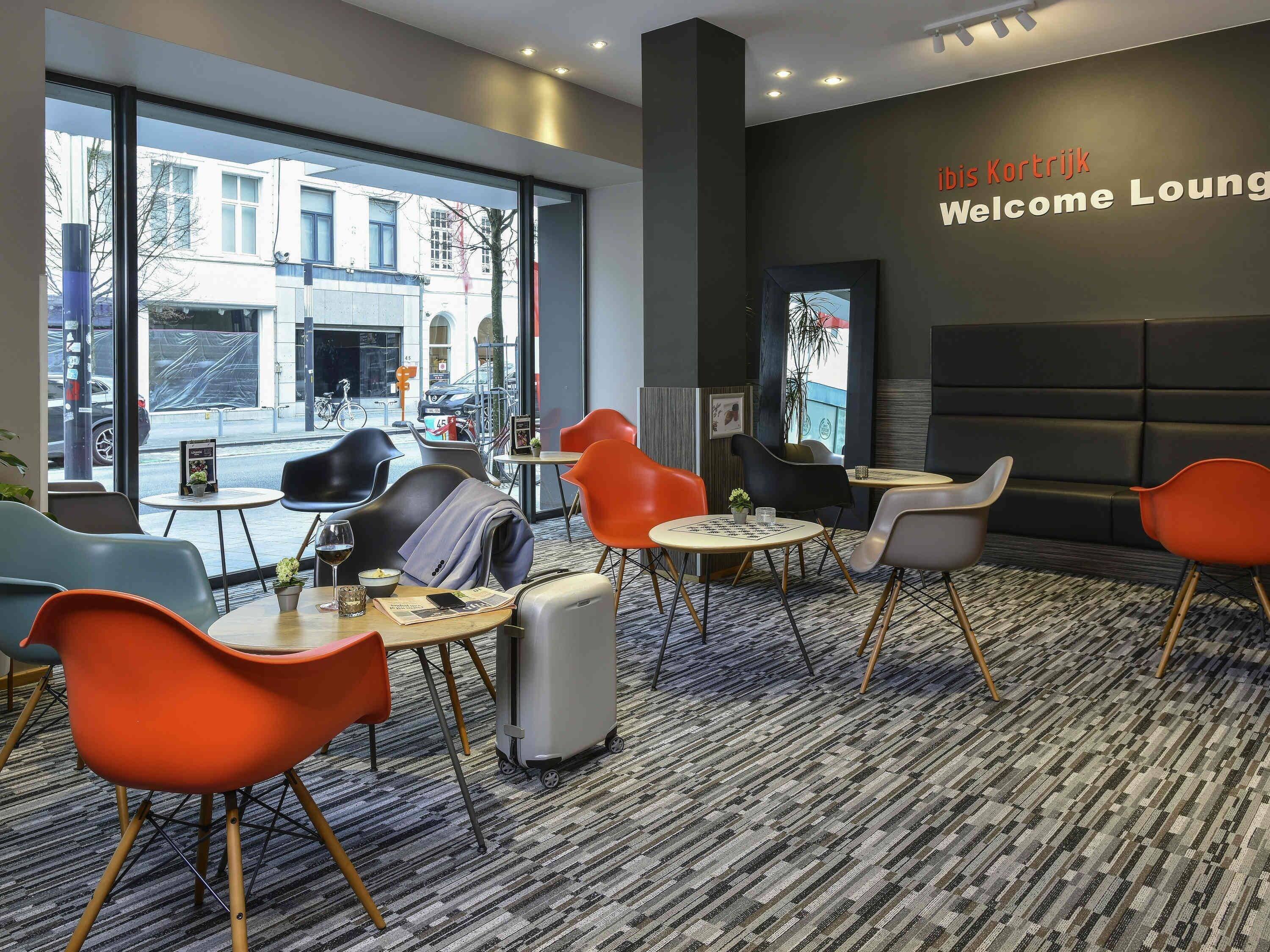 A modern lounge with a large window, a 'Welcome Lounge' sign, and a variety of seating options including chairs and tables.