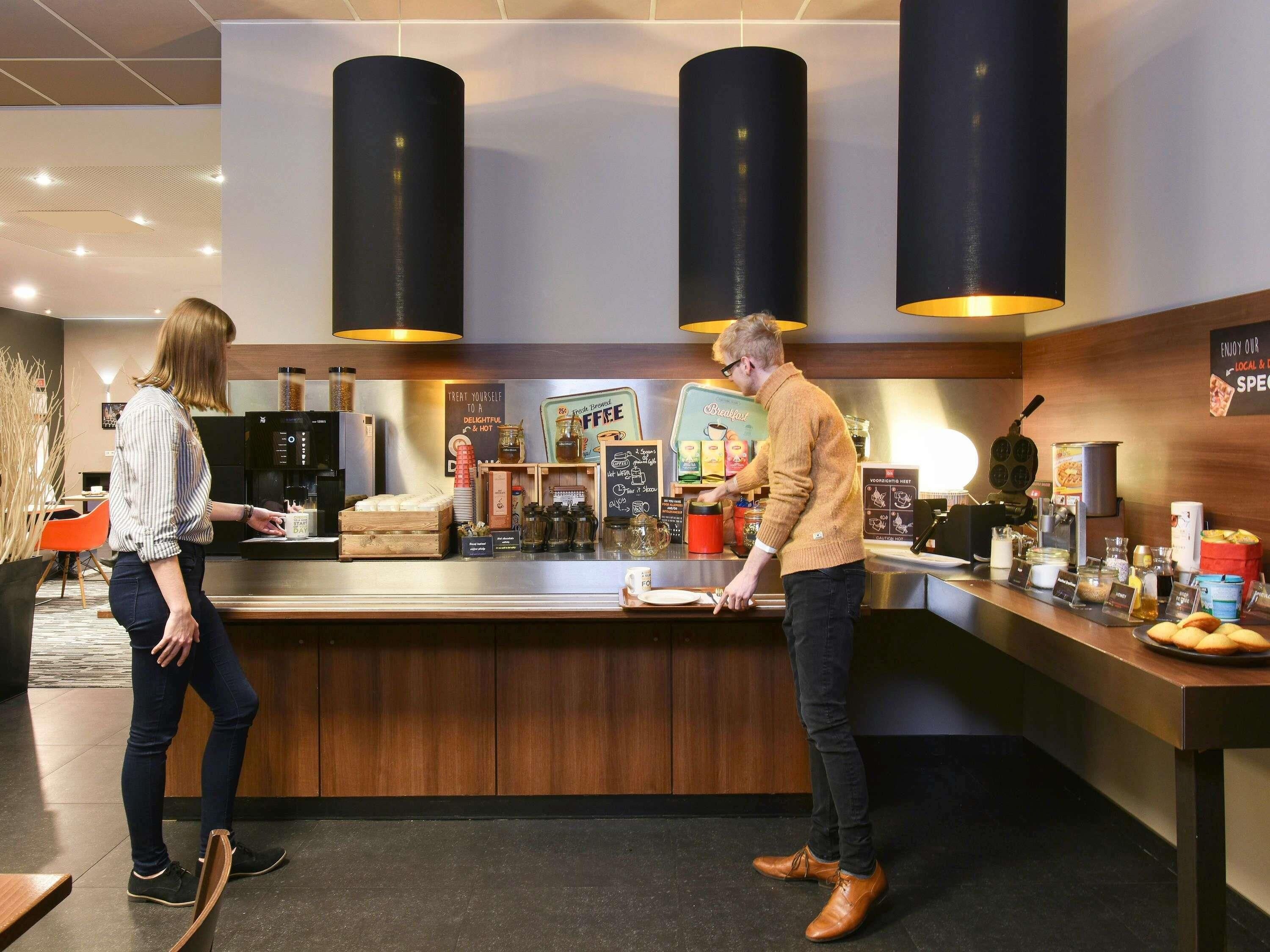 Een koffiebar toonbank met een barista die een drankje bereidt, een klant aan de bar, en diverse koffiezetapparatuur en benodigdheden.