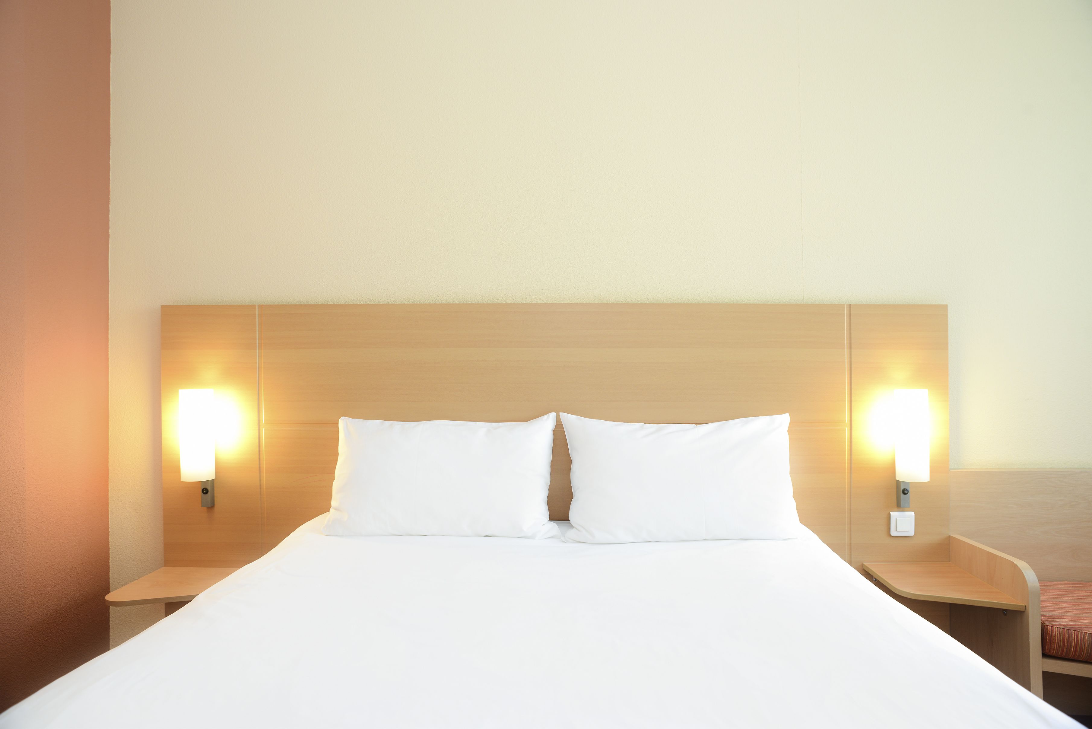 A hotel room with a large bed, two bedside tables, and wall-mounted lamps.