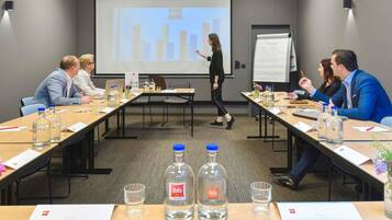Ein Konferenzraum mit Präsentationsschirm, Whiteboard und einem Tisch mit Wasserflaschen und Dokumenten.