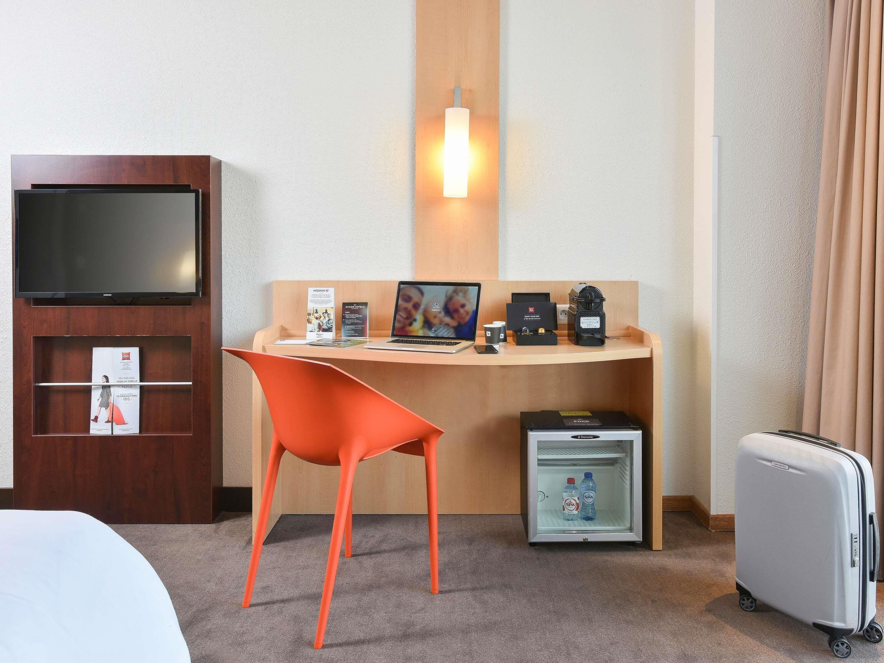 Une chambre d’hôtel équipée d’un bureau, d’une chaise, d’une télévision et d’un petit réfrigérateur.