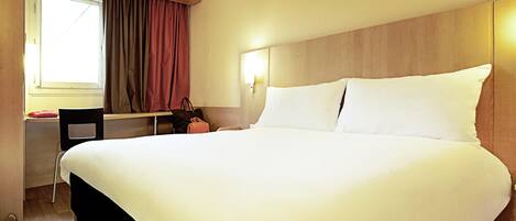 A hotel room with a large bed, a desk, and a chair.