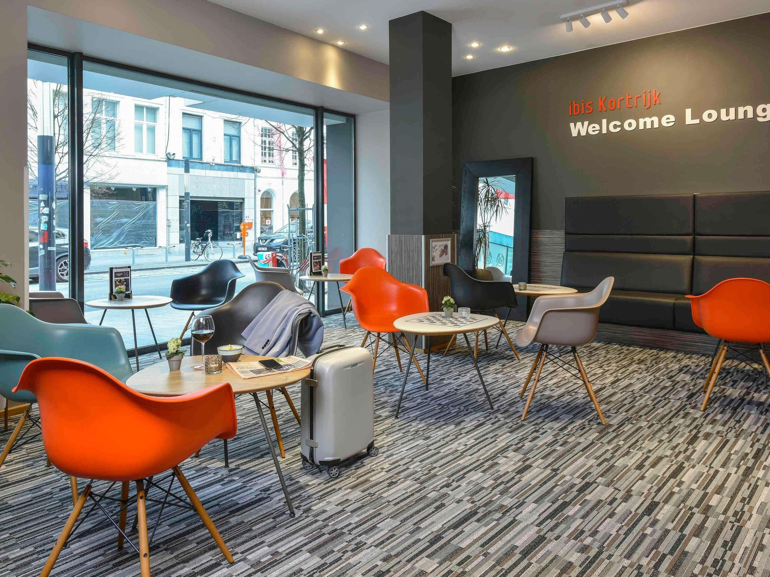 Una moderna lounge con vista sulla strada, sedute confortevoli e un cartello con la scritta 'Welcome Lounge'.