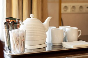 Una bandeja con una tetera blanca, varias tazas blancas, un vaso con una bolsita de té y una servilleta.
