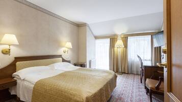 A hotel room with a large bed, two bedside lamps, a desk with a chair, and a television.