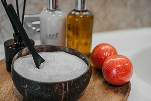 A wooden bowl filled with white granules, two red spherical objects, and two bottles with labels on a wooden surface.