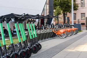 A row of electric scooters parked on a sidewalk with a building in the background.