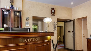 A reception area with a wooden counter labeled "RECEPTION," a clock on the wall, and a lamp. - Rinno hotel (Vilnius)