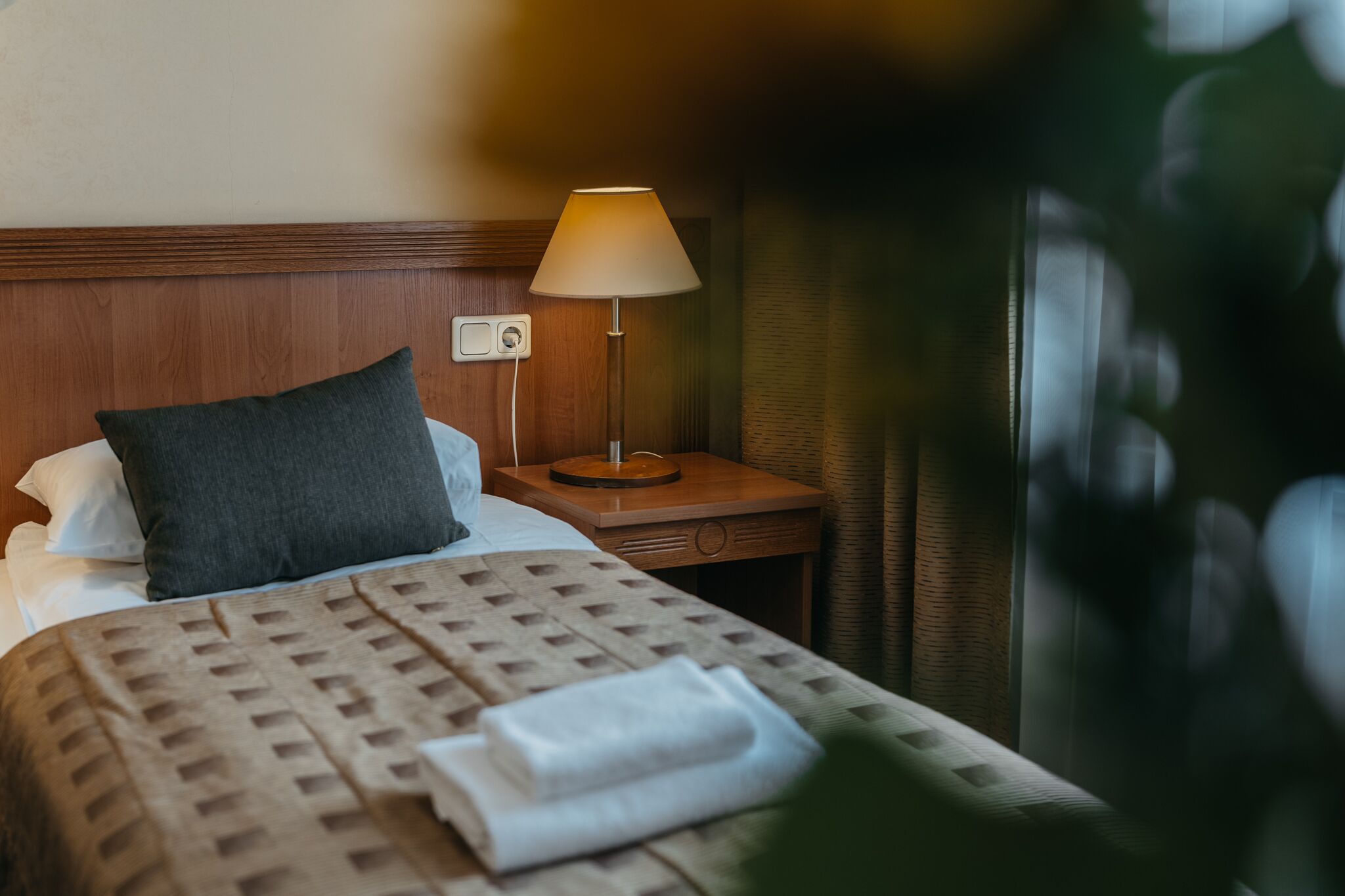 Quarto de hotel com uma cama, mesa de cabeceira com abajur e tomada.