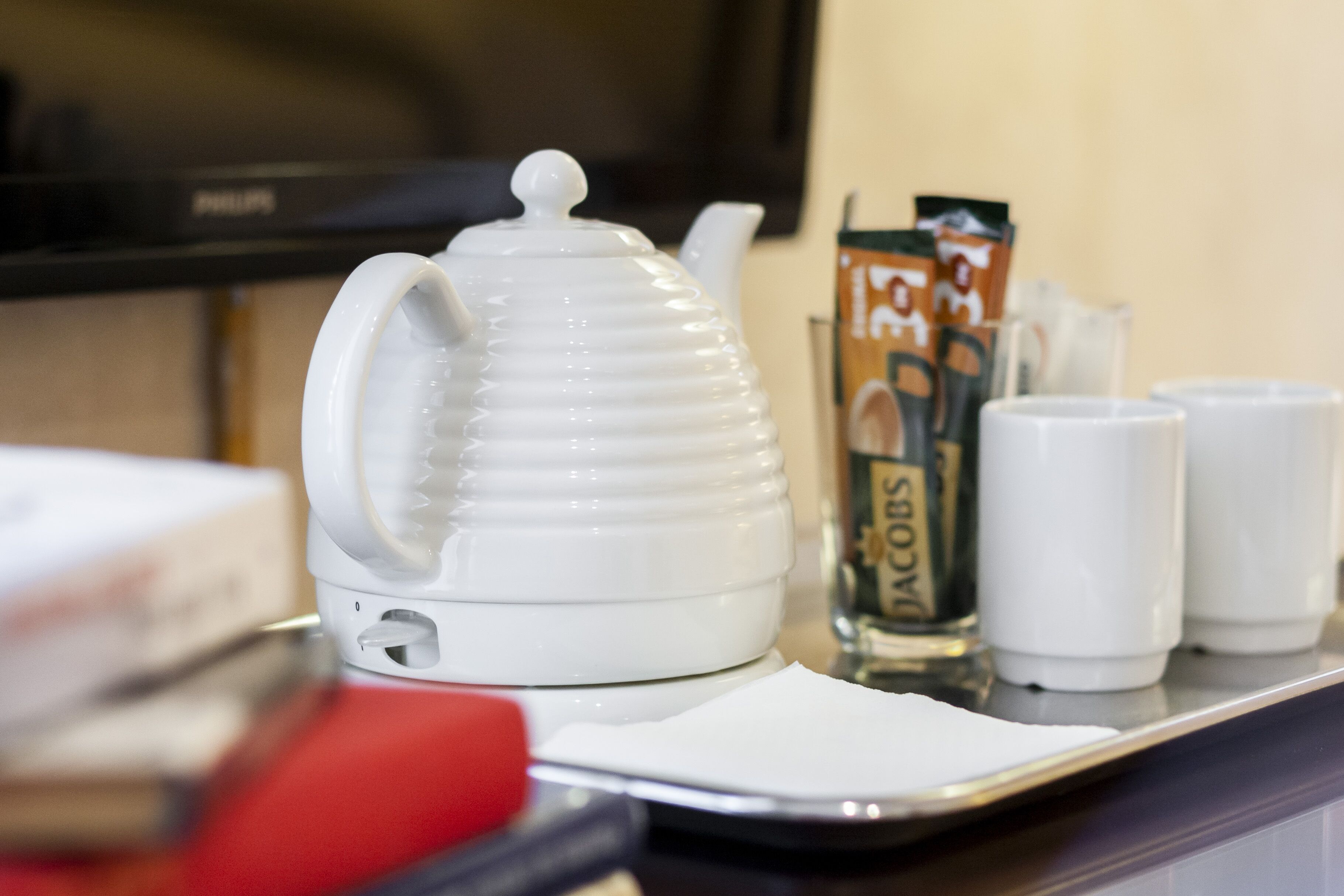 A white teapot on a tray with two white cups and a box of Jacobs coffee.
