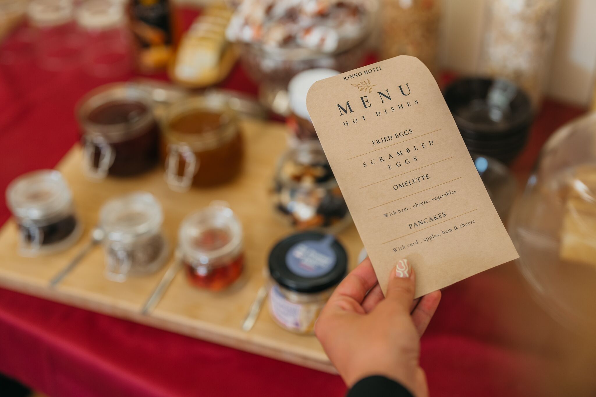 A hand holding a menu card with items like fried eggs, scrambled eggs, omelette, and pancakes.