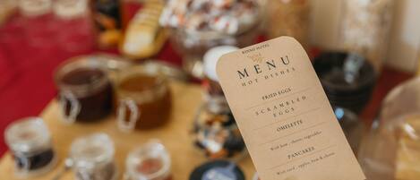 A hand holding a menu card with items like fried eggs, scrambled eggs, omelette, and pancakes.