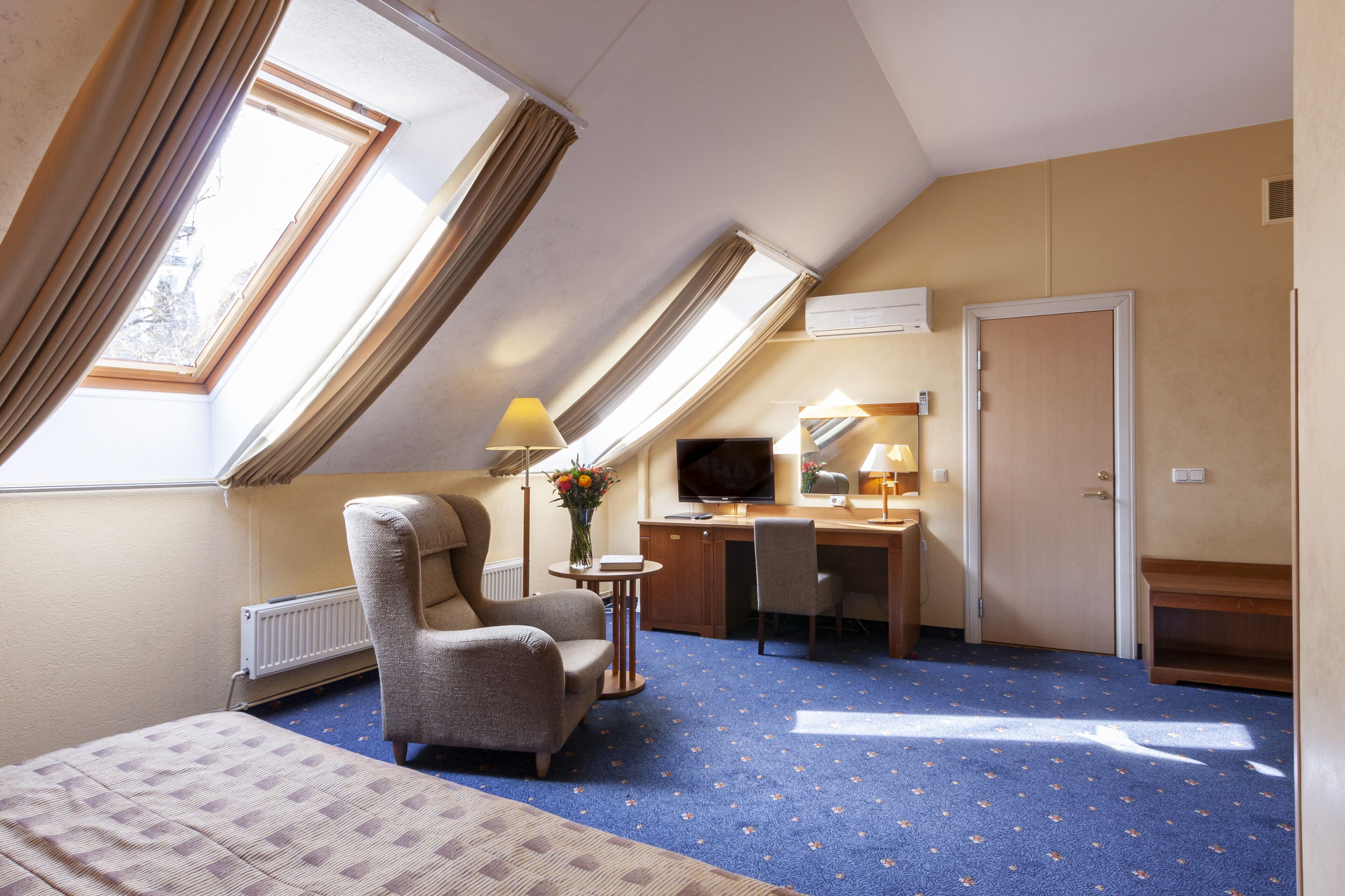 A hotel room with a bed, a desk, a chair, a television, and a window with curtains.