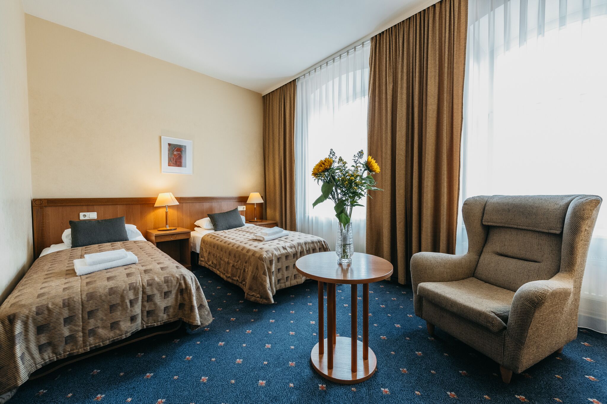 Ett hotellrum med två sängar, ett runt bord, en stol och en vas med blommor.