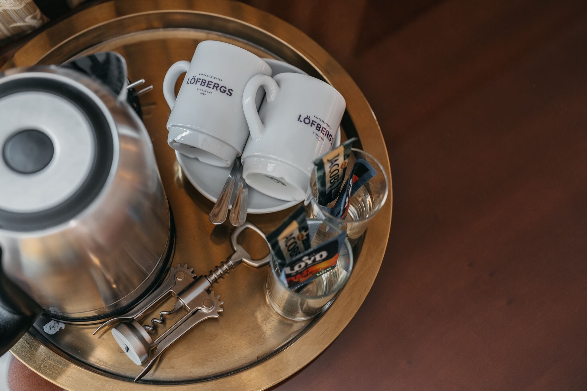 A tray with two white coffee mugs, a silver teapot, a bottle of water, and a bottle of coffee creamer.