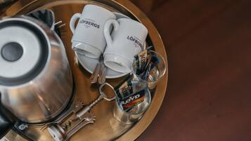 A tray with two white coffee mugs, a silver teapot, a bottle of water, and a bottle of coffee creamer.