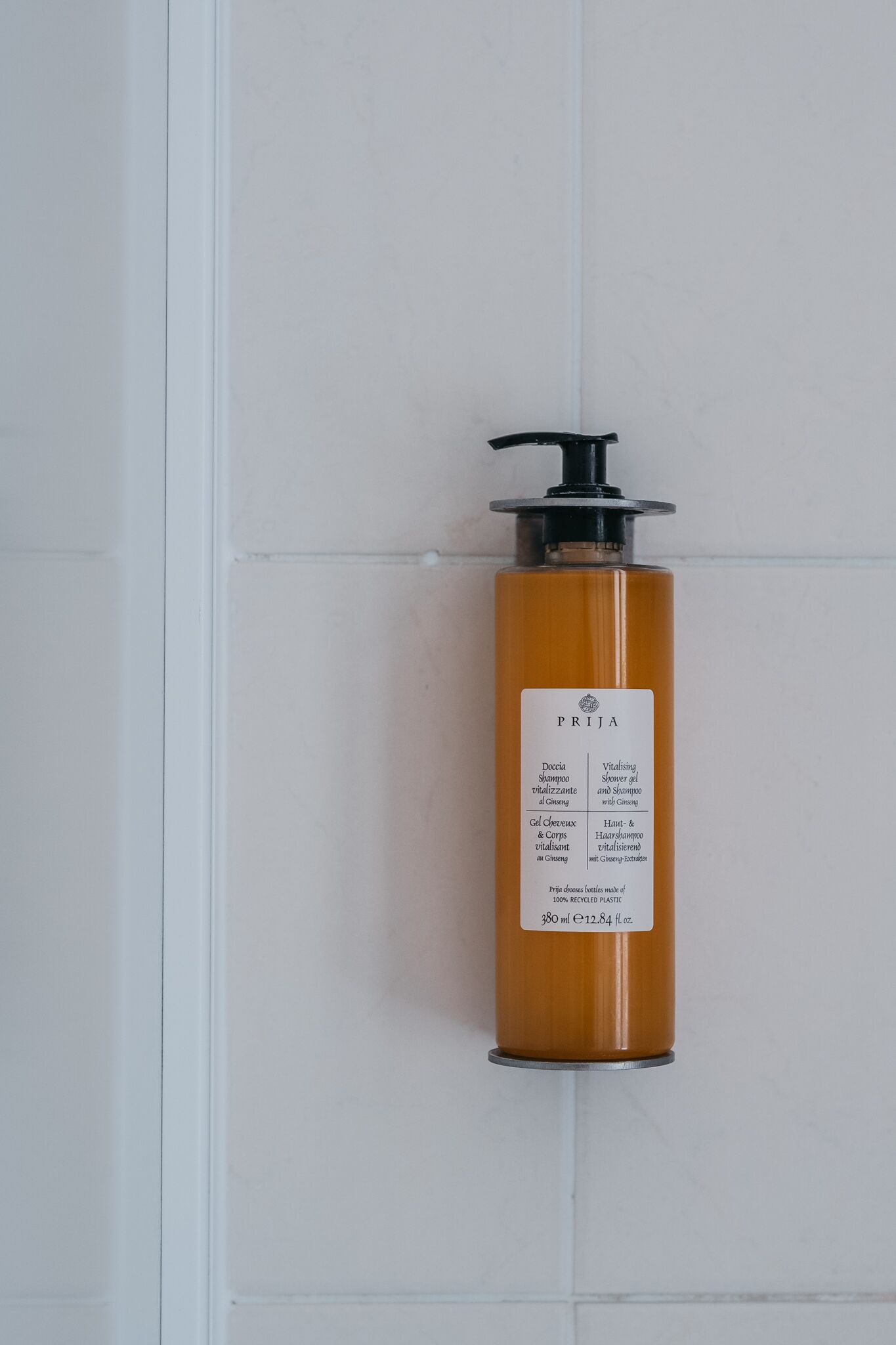 A bottle of PRIJA shower gel on a white tiled wall.