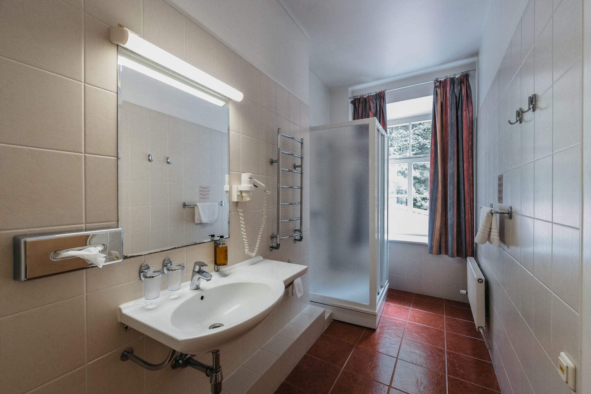 Een badkamer met een wastafel, spiegel, handdoekhouder en douche.