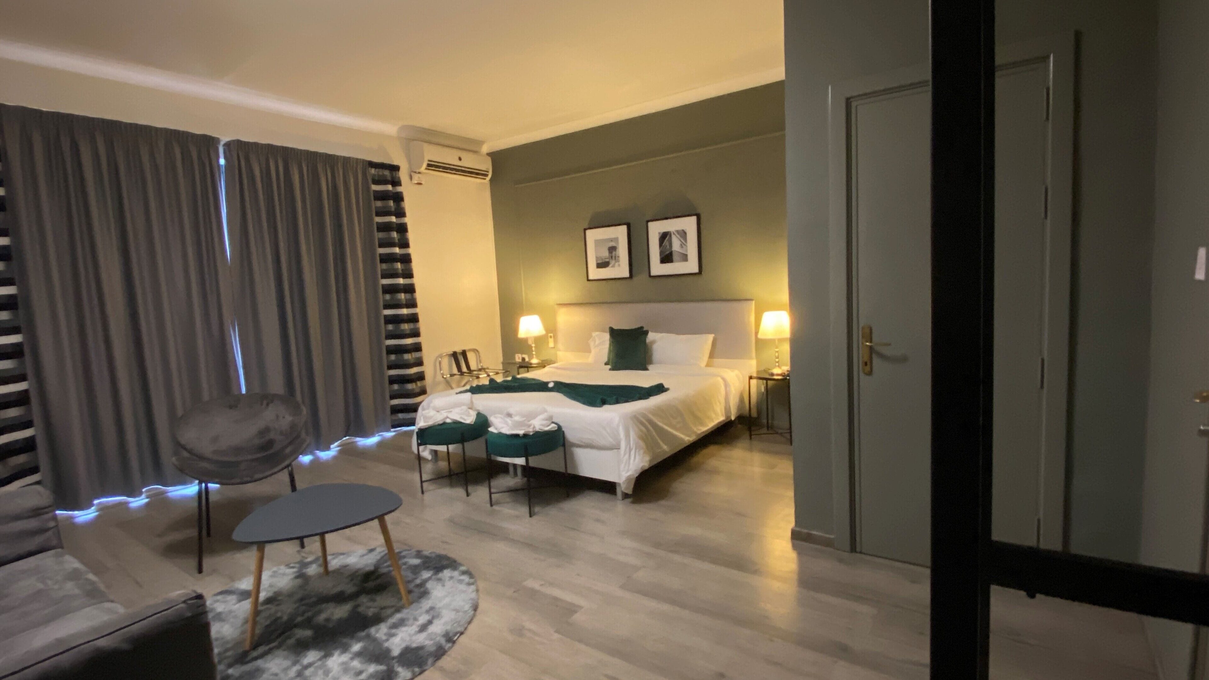 A hotel room with a bed, bedside tables, a chair, a small table, and a door.