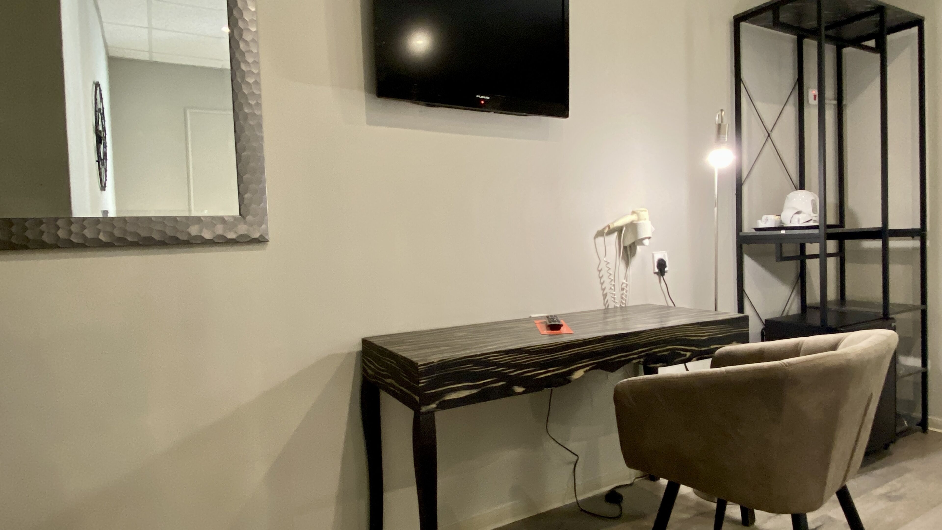 Una habitación moderna con un escritorio de madera oscura, una silla, un televisor de pantalla plana, un espejo y una estantería negra.