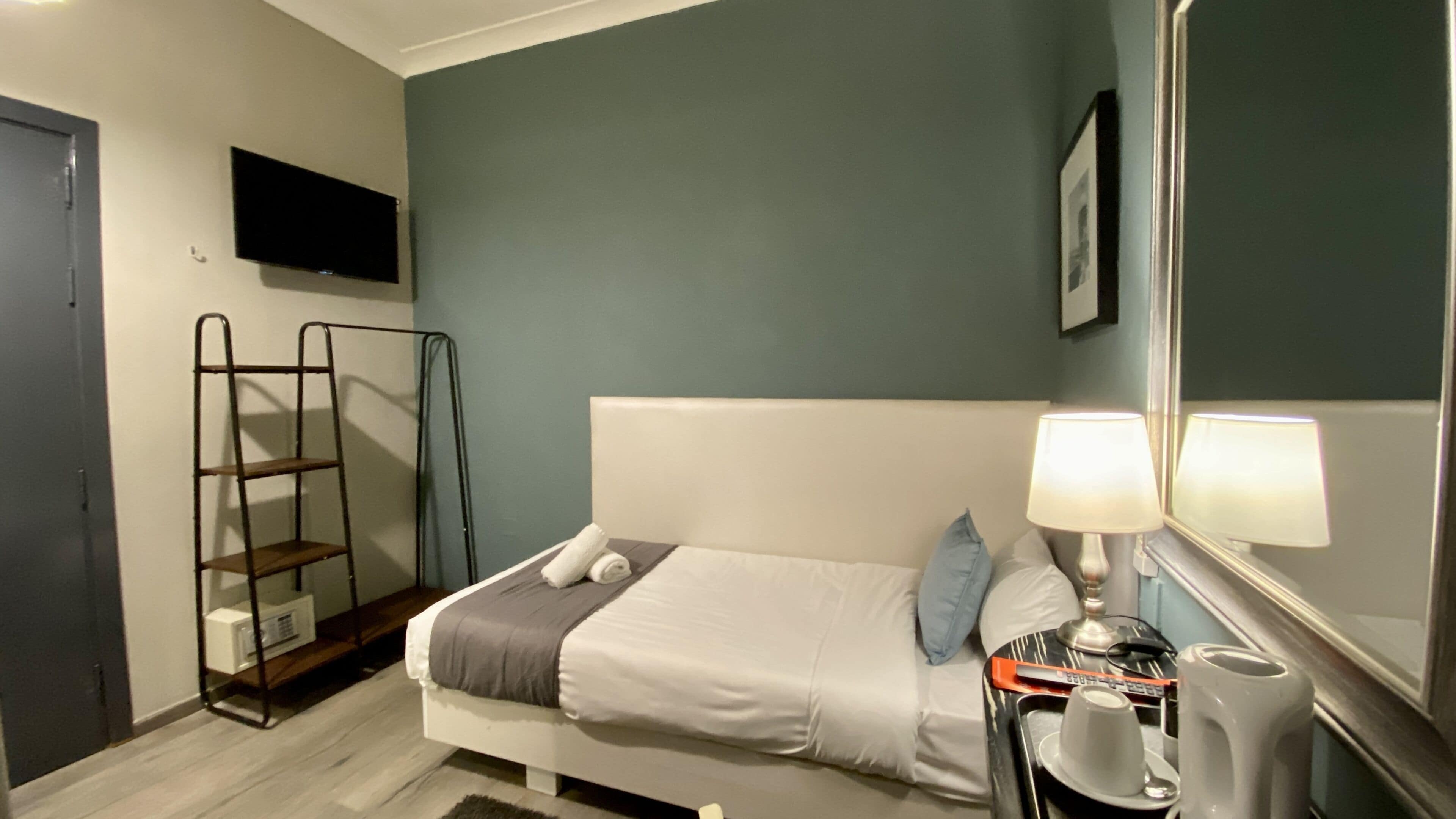 A bedroom with a bed, a bedside table with a lamp, a TV mounted on the wall, and a ladder against the wall.