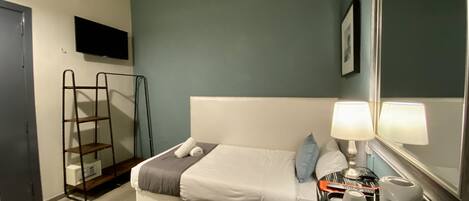 A bedroom with a bed, a bedside table with a lamp, a TV mounted on the wall, and a ladder against the wall.