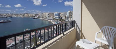 A balcony with a view of a coastal cityscape, including a marina with boats and a road with vehicles.