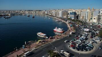 A coastal cityscape with a marina, boats, and a busy road with parked cars.
