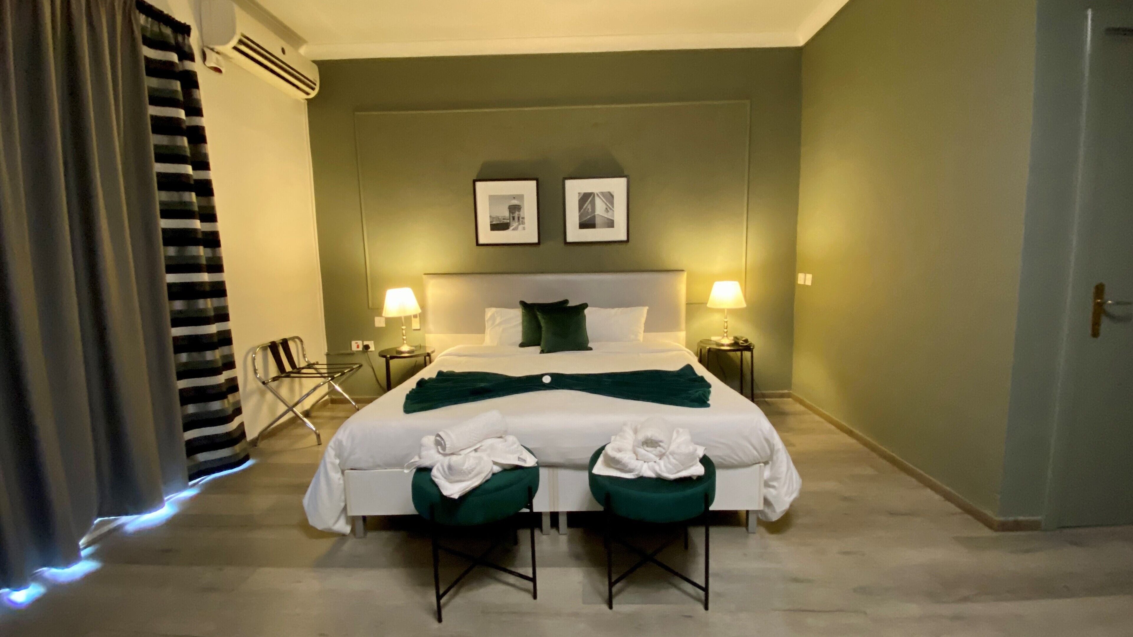 A hotel room with a large bed, two bedside tables with lamps, a chair, and a door.