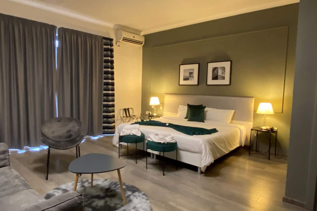Hotellihuone, jossa on sänky, kaksi yöpöytävalaisinta, tuoli, pieni pöytä ja suuri ikkuna, jossa on verhot.