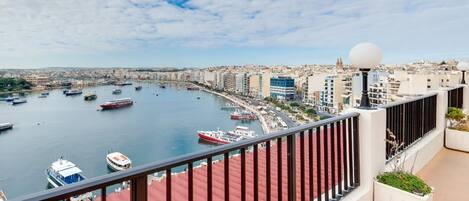 Un paisaje urbano costero con un puerto deportivo lleno de barcos, edificios modernos y cielo despejado.