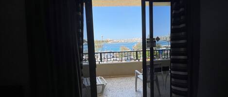 A room with a sliding glass door leading to a balcony with a view of the sea and a cityscape.