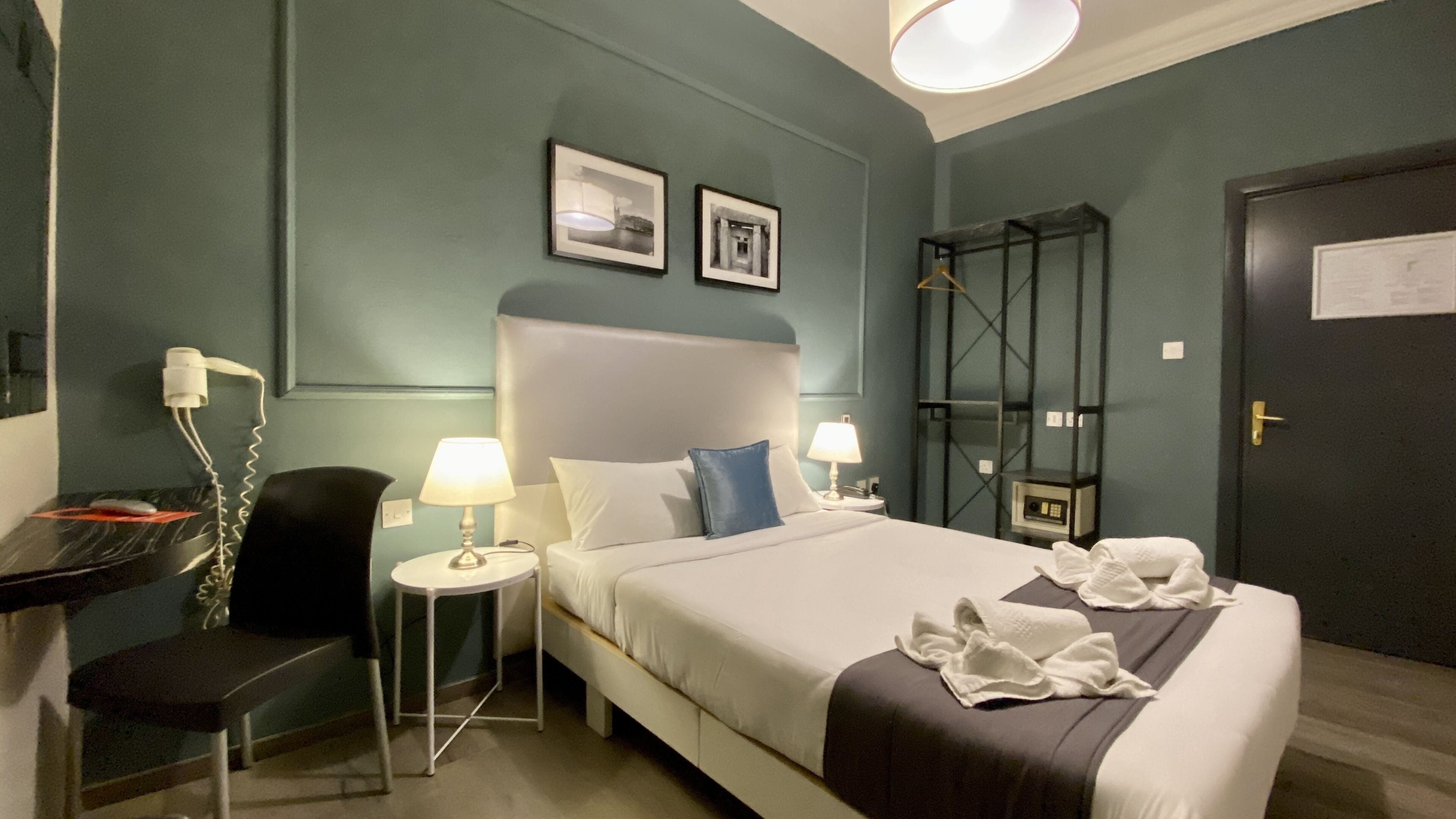 A hotel room with a bed, two bedside tables, a chair, a desk, and a wardrobe.