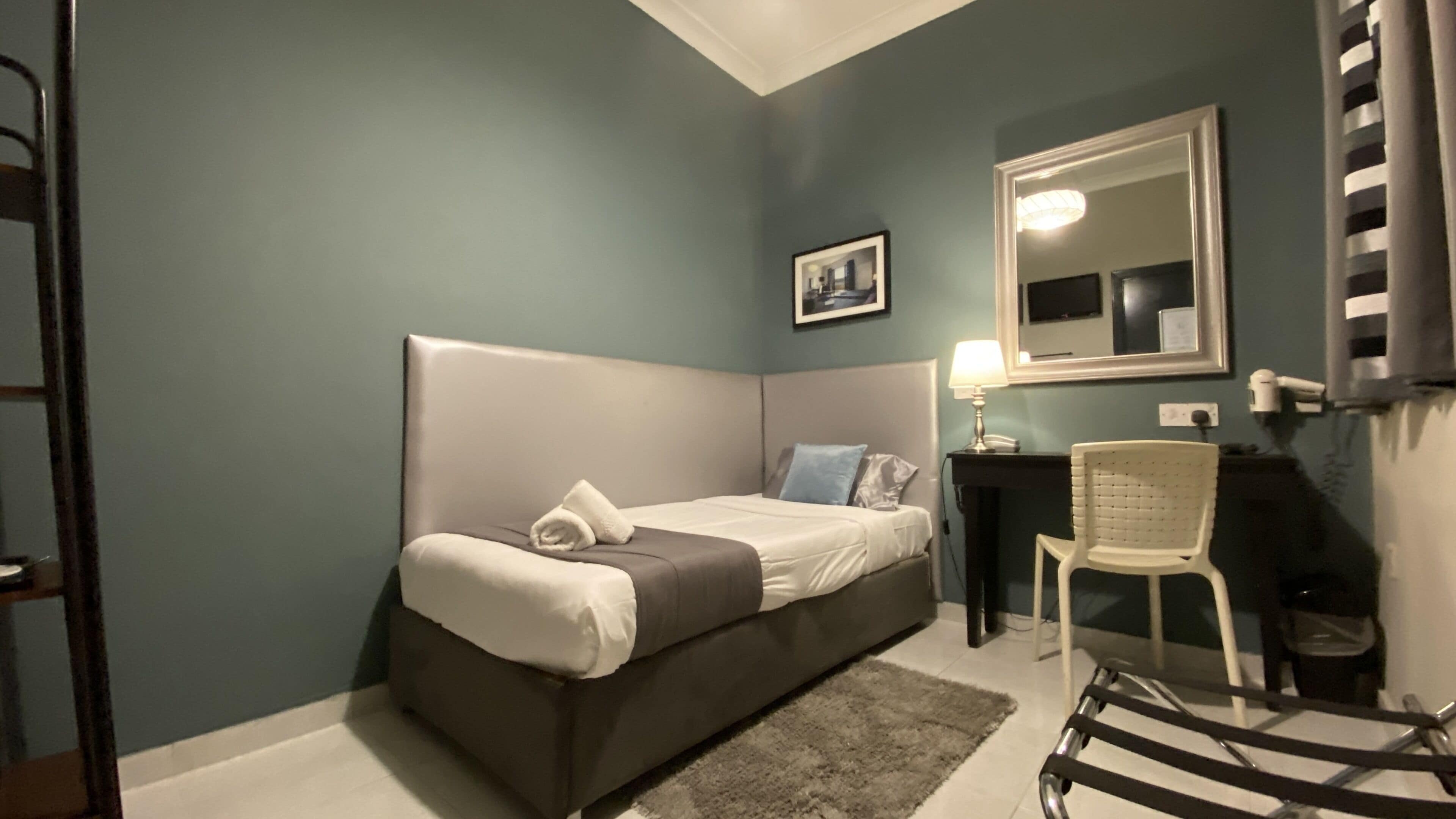 Un dormitorio con cama, una silla, un escritorio, un espejo y una lámpara.