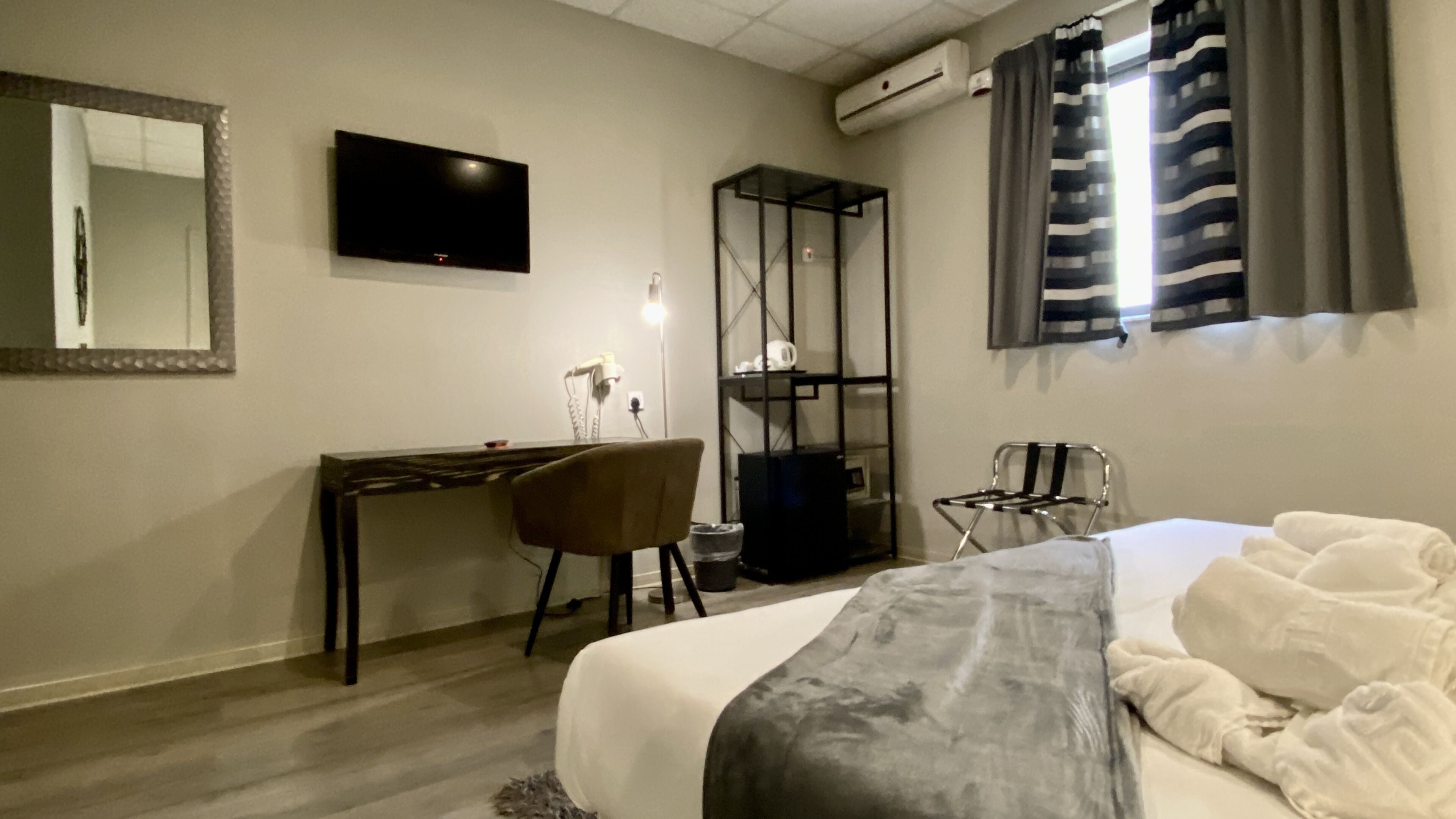 Ett hotellrum med en säng, ett skrivbord, en stol, en tv och en hylla.