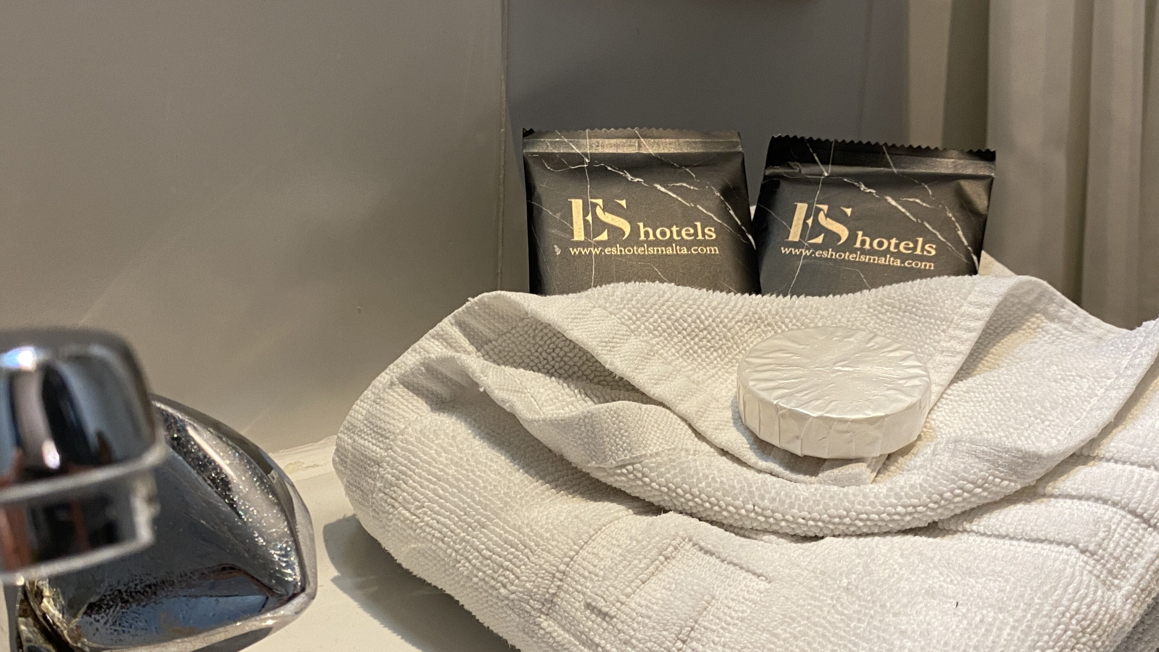 A bathroom with a towel, a bar of soap, and two toiletries bags labeled 'Eshotels'.