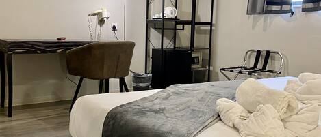 A hotel room with a bed, a desk, a chair, a small table, a shelf, and a window with curtains.