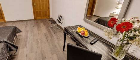 A hotel room with a bed, a dining table with fruit and flowers, a chair, and a large mirror.