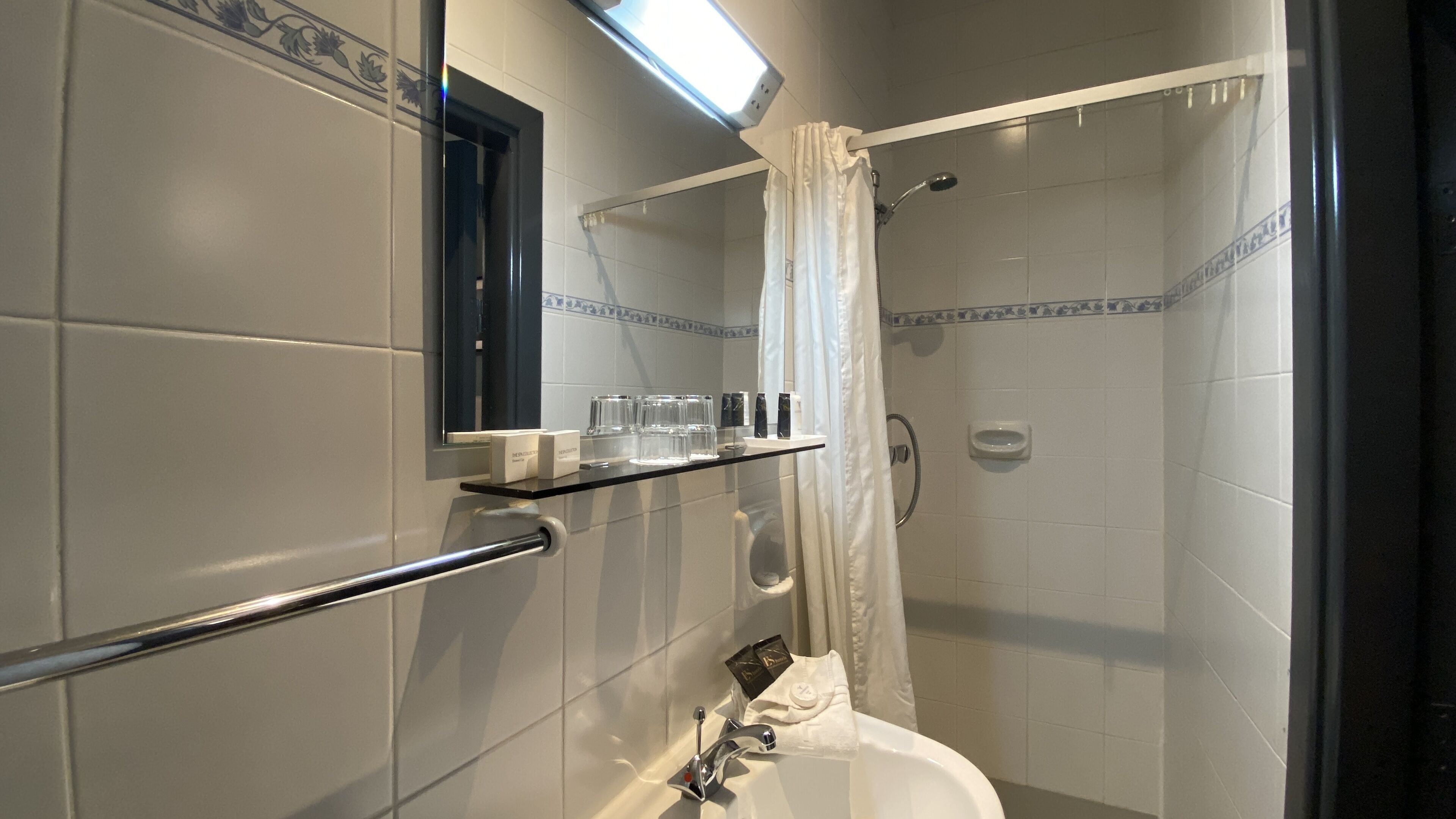 Un baño con ducha, lavamanos, espejo y repisa con artículos de aseo.