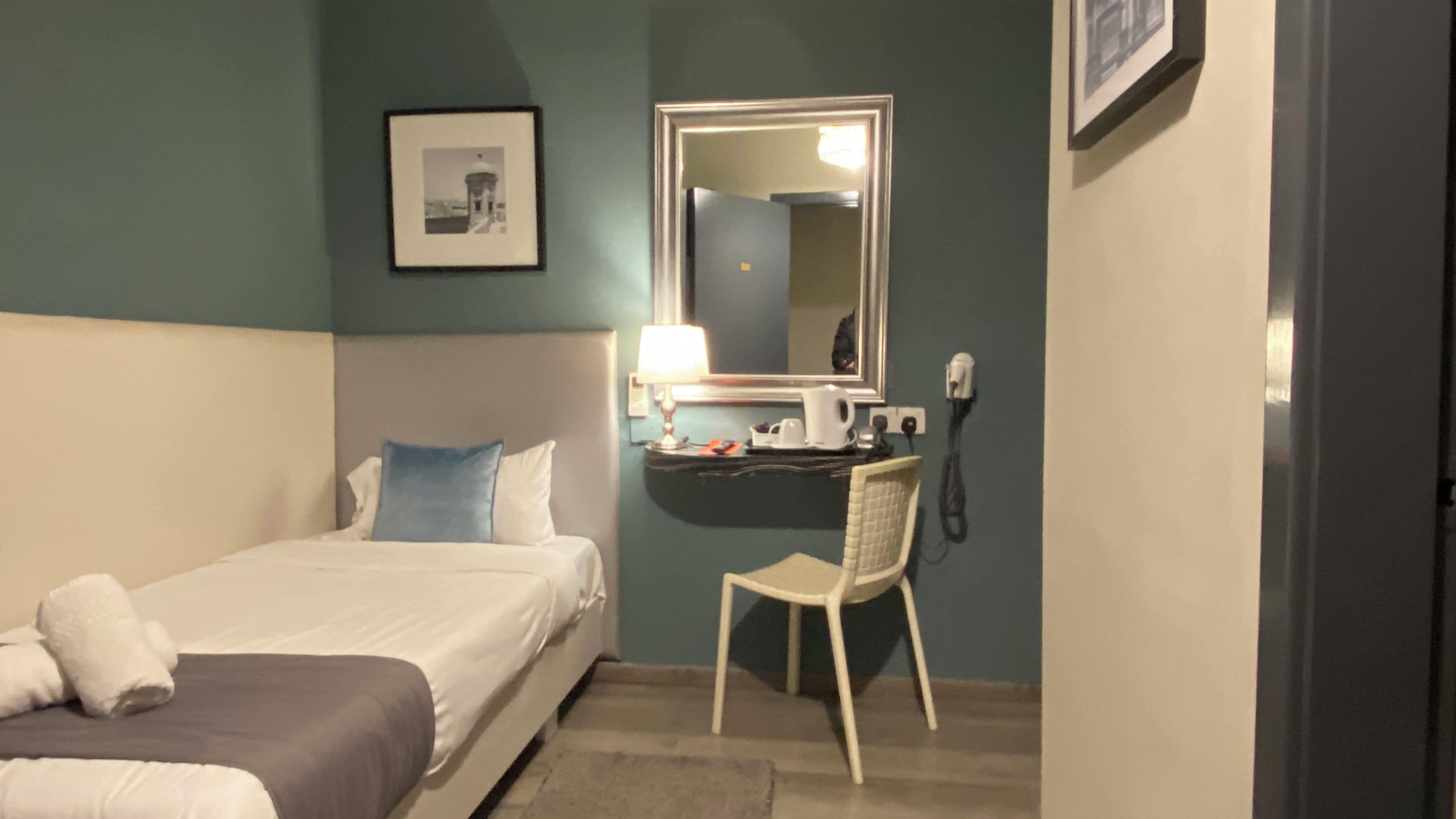 Une chambre d’hôtel avec un lit, un bureau, une chaise, une lampe et un tableau encadré au mur.